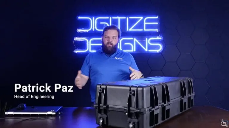 Patrick Paz, Head of Engineering at Digitize Designs, presenting beside a 3D scanner case in front of the neon Digitize Designs sign