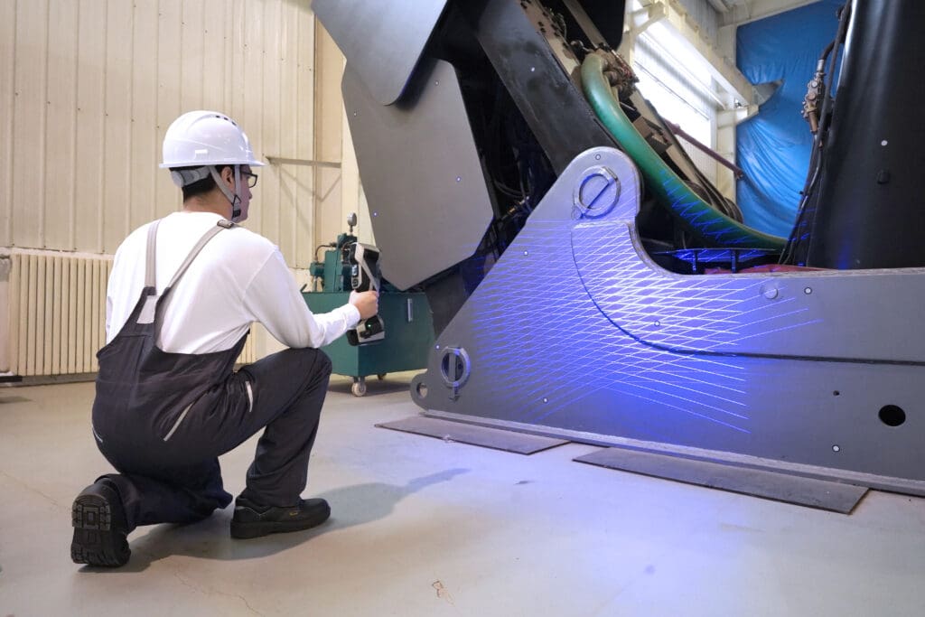 A man using a Scantech KSCAN X handheld 3D scanner to measure large machinery, demonstrating ultra-large part scanning.