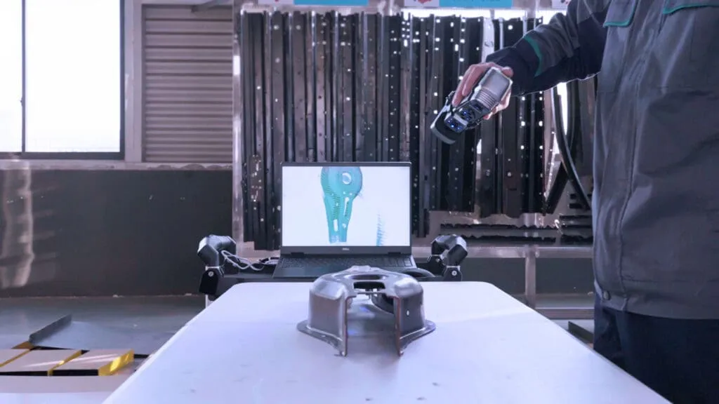 Technician 3D scanning a part using the simscan-s gen 2 3d scanner, with a monitor displaying the live scan model in the background.