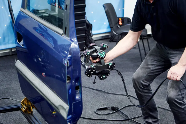 Engineer 3D scanning a blue car door with a handheld scanner fitted with tracking targets