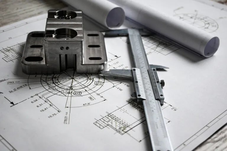 Machined steel part and a caliper resting on an engineering drawing with dimensions