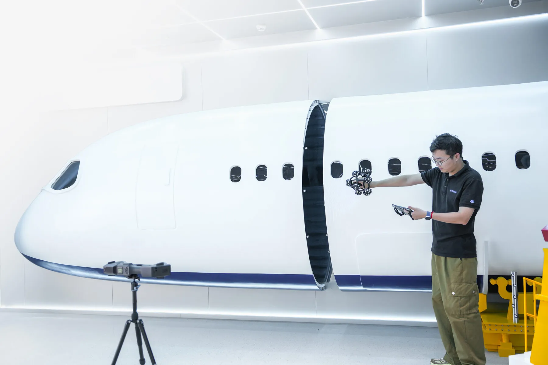 TrackScan GO tracker on a tripod measuring an aircraft fuselage section while an operator scans alongside it