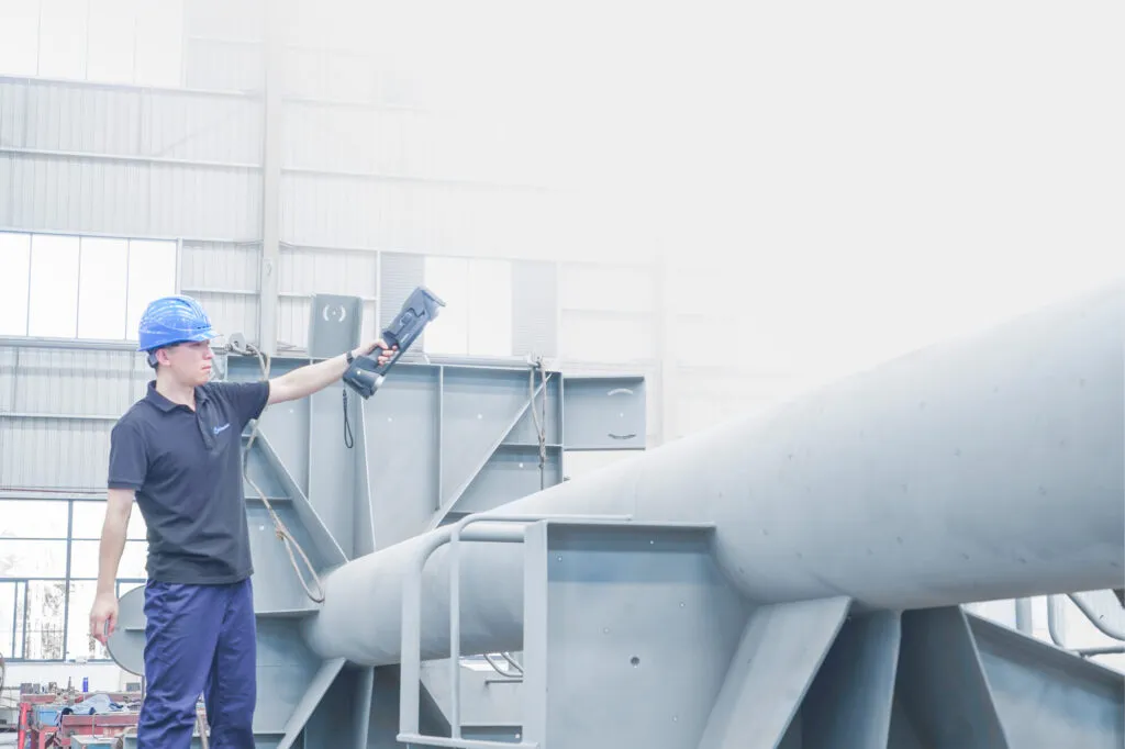 Technician operating the TrackScan GO from a handheld tablet beside a large fabricated structure, working without a laptop or cables