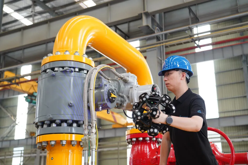 Technician in a hard hat scanning a yellow industrial valve assembly with the TrackScan Sharp-Z handheld scanner